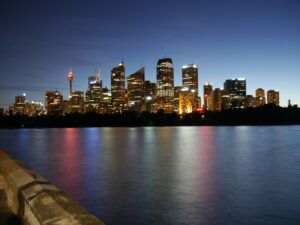 a city skyline with lights reflecting on water showing Sydney CBD